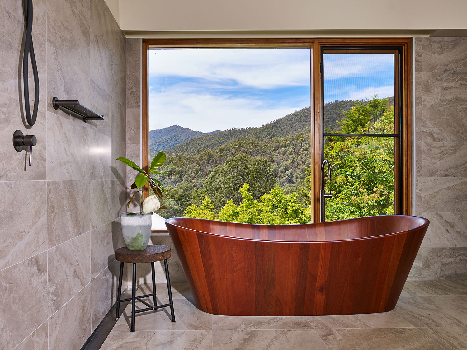 A beautifully polished red gum soaker bath faces a large glass-panelled window